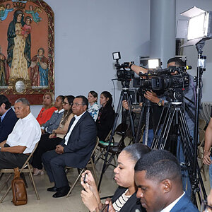 An audience watches as cameras are set up near a religious icon.